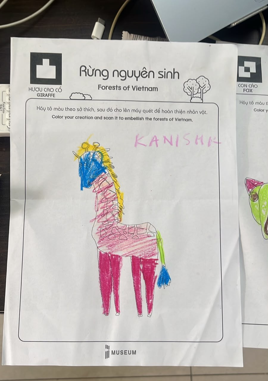 A museum coloring sheet of a giraffe colored with a blue face, yellow mane and pink body, with KANISHK handwritten in pink